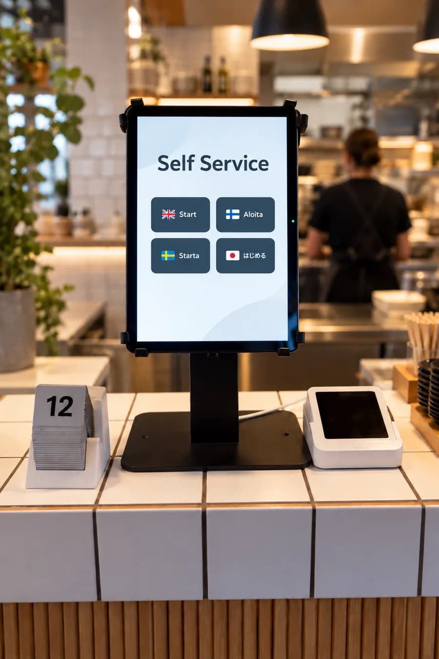 Self-service ordering tablet on a cafe counter, showing the language picker with English, Finnish, Swedish and Japanese